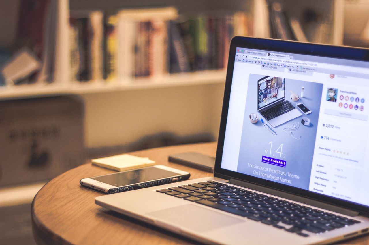 About A cozy modern workspace featuring a laptop displaying a website, a smartphone, and books on shelves.